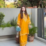 A mustard yellow 3-piece embroidered cotton suit with a Munaar dupatta, featuring white lace detailing on the sleeves and hem Lubaba Luxury.