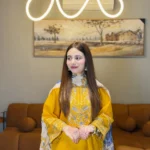 A mustard yellow 3-piece embroidered cotton suit with a Munaar dupatta, featuring white lace detailing on the sleeves and hem Lubaba Luxury.