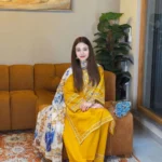 A mustard yellow 3-piece embroidered cotton suit with a Munaar dupatta, featuring white lace detailing on the sleeves and hem Lubaba Luxury.